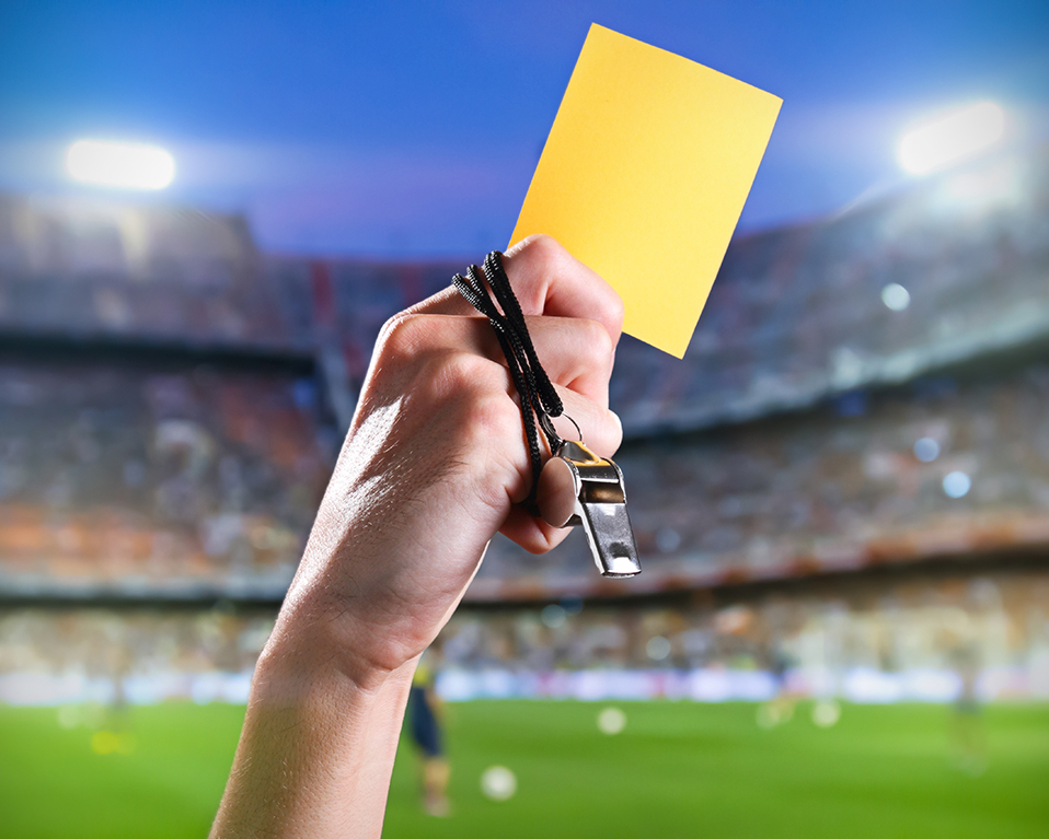 Árbitro de fútbol con un silbato en la mano, mostrando una tarjeta amarilla en un estadio repleto de gente